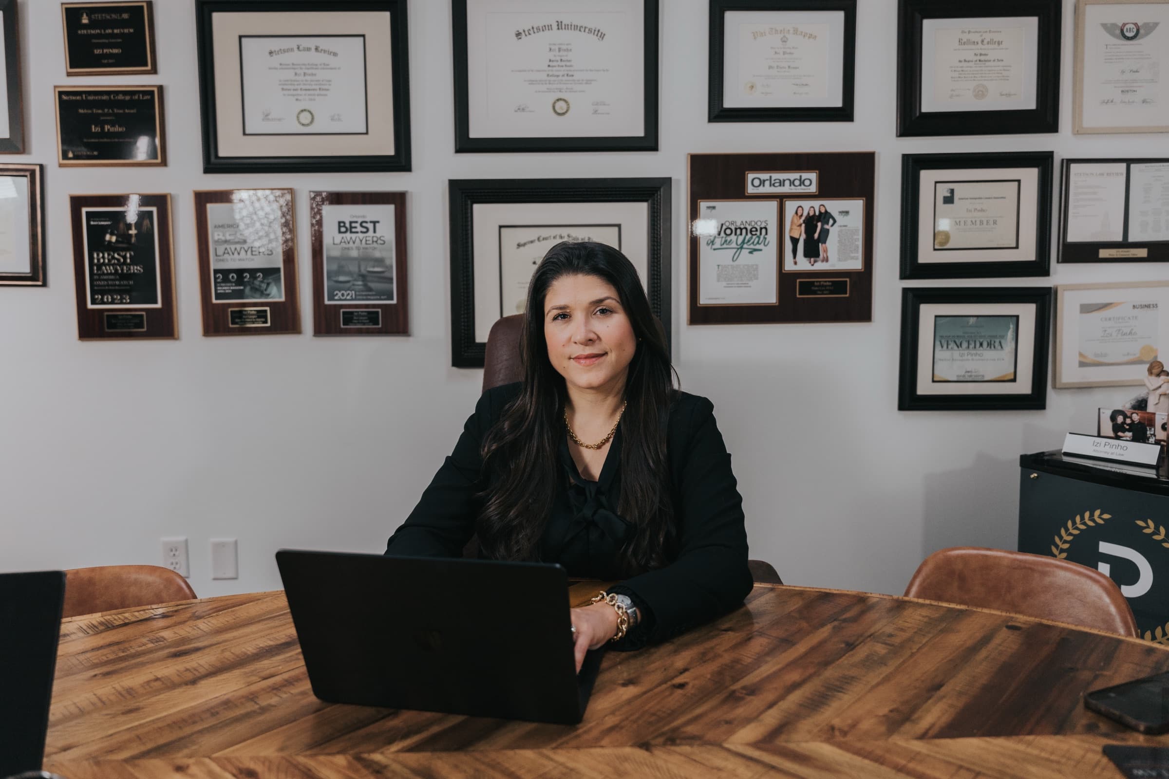 Dra. Izi Pinho at her Orlando office — credentials wall visible behind her.