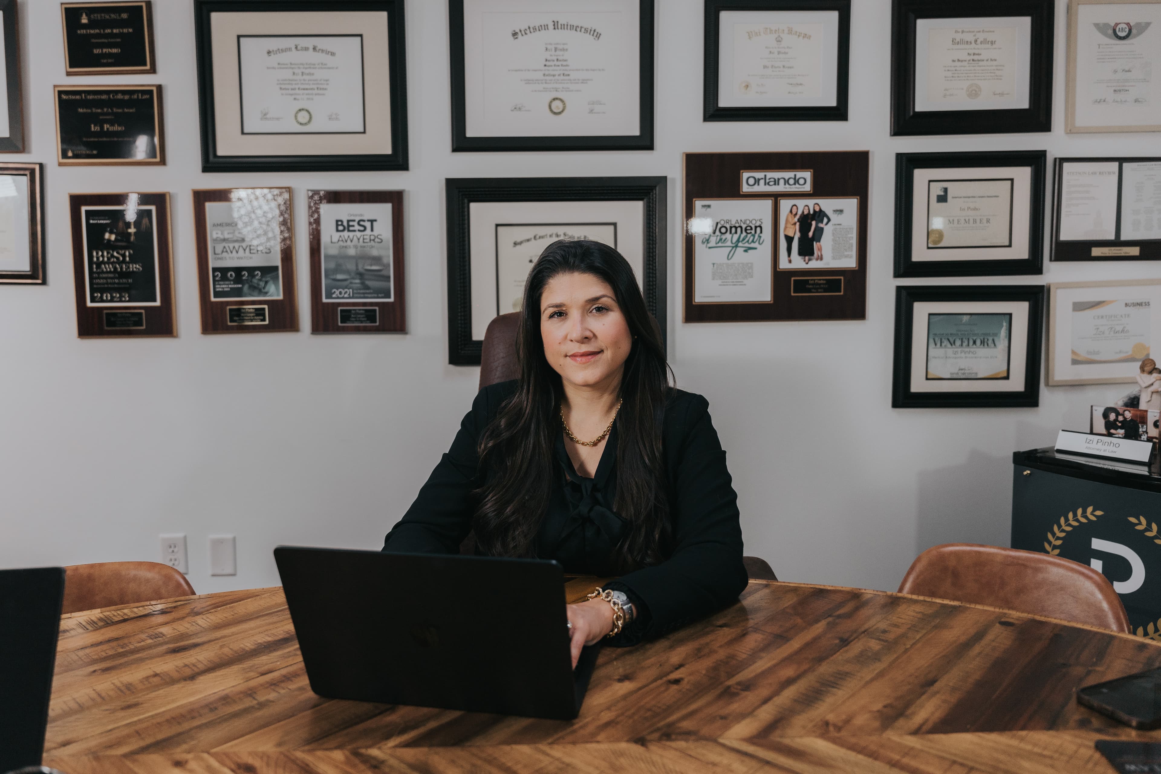Dra. Izi Pinho at her Orlando office — credentials wall visible behind her.